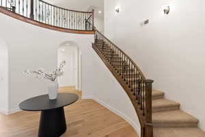 Staircase featuring wood finished floors, arched walkways, baseboards, and a high ceiling
