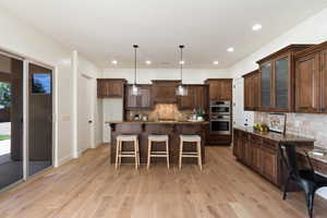 Kitchen featuring stainless steel double oven, decorative backsplash, a breakfast bar, light wood-style flooring, and glass insert cabinets
