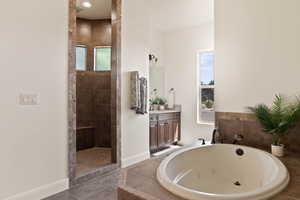 Bathroom with a tub with jets, baseboards, walk in shower, and vanity
