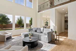 Living room featuring a towering ceiling, healthy amount of natural light, a chandelier, light wood-type flooring, and baseboards