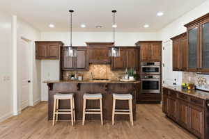 Kitchen featuring stainless steel double oven, premium range hood, tasteful backsplash, a breakfast bar area, and recessed lighting