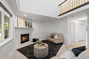 Living room with soaring ceilings, custom wainscot, light carpeted flooring, and corner fireplace with tile surround