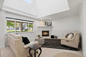 Living room with soaring ceilings, custom wainscot, light carpeted flooring, and corner fireplace with tile surround