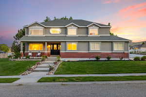 View of front of home featuring brick wainscot, stucco siding, a yard, and a covered porch