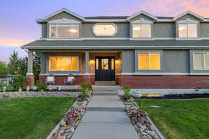 View of front of home featuring brick wainscot, stucco siding, a yard, and a covered porch
