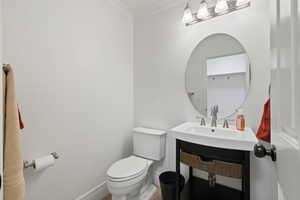 Bathroom with toilet, crown molding, baseboards, and a sink