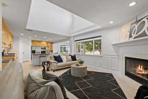 Living room with soaring ceilings, custom wainscot, light carpeted flooring, and corner fireplace with tile surround