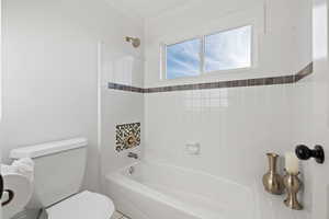 Full bathroom with toilet and tub-shower combo with tile surround