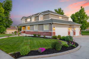 View of front of house featuring brick wainscot, a 3-car garage, stucco exterior, concrete driveway, and a front lawn with flower beds