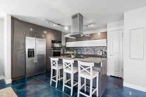 ADU kitchen with stainless steel appliances, island range hood, finished concrete flooring, decorative backsplash, and recessed lighting