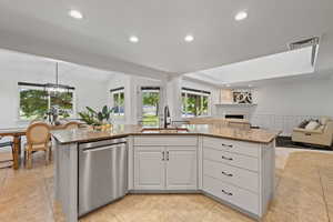 View of kitchen island with warm neutral painted finish, stainless steel dishwasher, workstation sink, and quartz countertops