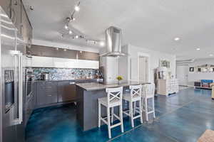 ADU kitchen with stainless steel appliances, island range hood, finished concrete flooring, decorative backsplash, and recessed lighting