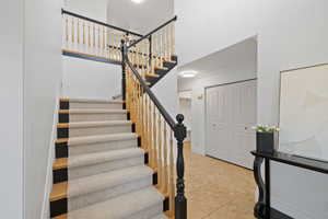 Turned stairwell with custom wood railing, patterned carpet runner, and tile entry.