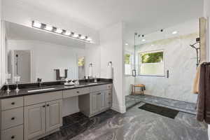 Primary bathroom featuring double vanity with quartz countertops, marbled tile flooring, and a walk-in shower with euro-glass and dual showerheads