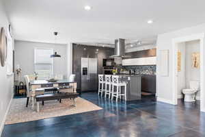 ADU kitchen with stainless steel appliances, island range hood, finished concrete flooring, decorative backsplash, and recessed lighting