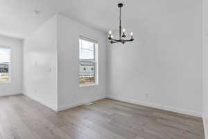 Empty room with a chandelier, light wood finished floors, baseboards, and a smoke detector