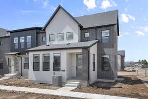 View of front facade with cooling unit, brick siding, and roof with shingles