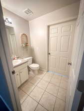 Half bath with tile patterned flooring, toilet, vanity, and a textured ceiling