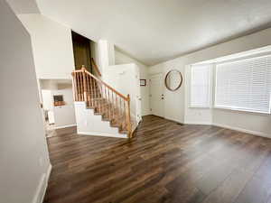 Foyer with vaulted ceiling, wood finished floors, stairway, and baseboards