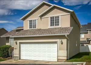 View of front facade with stucco siding, fence, an attached garage, and roof with shingles
