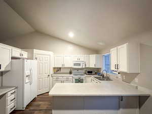 Kitchen featuring white appliances, lofted ceiling, a sink, a peninsula, and dark wood-type flooring