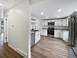 Kitchen with appliances with stainless steel finishes, a sink, open shelves, recessed lighting, and light wood-style floors