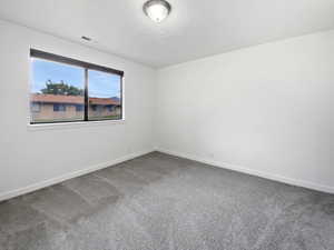 Spare room featuring dark colored carpet and baseboards