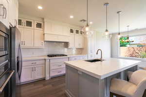 Kitchen featuring a sink, a kitchen bar, dark wood-style floors, tasteful backsplash, and gas stovetop