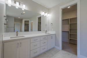 Bathroom featuring a walk in closet, marble look tile flooring, double vanity, baseboards, and recessed lighting