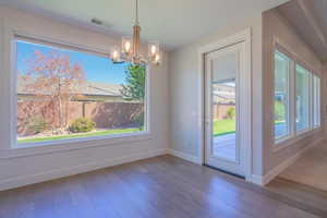 Unfurnished dining area featuring a chandelier, baseboards, wood-type flooring, and plenty of natural light