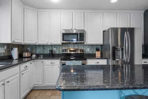 Open kitchen featuring granite countertop, stainless steel appliances and white cabinets