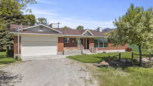 Ranch-style home with an attached garage, brick siding, a porch, dirt driveway, and a chimney