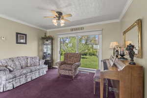 Carpeted living area featuring ornamental molding and a ceiling fan