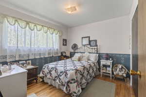 Bedroom featuring wallpapered walls, wood finished floors, and wainscoting