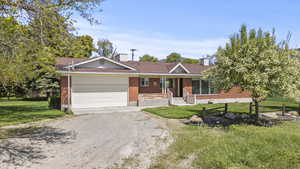 Single story home with a porch, dirt driveway, a garage, brick siding, and a front lawn