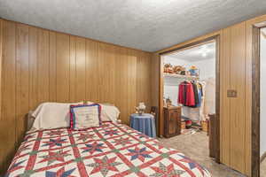 Bedroom featuring carpet floors, a walk in closet, wood walls, a closet, and a textured ceiling