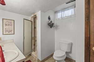 Bathroom featuring toilet, a stall shower, a textured ceiling, vanity, and tile patterned flooring