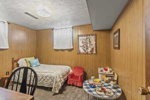 Carpeted bedroom featuring a textured ceiling and wooden walls