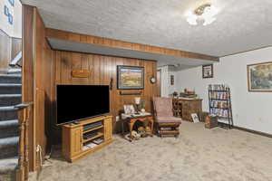 Living area with stairway, carpet floors, wood walls, a textured ceiling, and baseboards