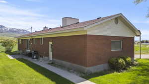View of side of home featuring entry steps, brick siding, a lawn, a chimney, and a mountain view