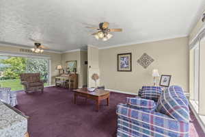 Living area featuring ceiling fan, carpet flooring, ornamental molding, and baseboards
