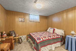Bedroom with carpet flooring, a textured ceiling, and wooden walls