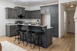Kitchen with appliances with stainless steel finishes, baseboards, light wood-style flooring, a kitchen bar, and recessed lighting