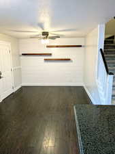 Unfurnished living room with baseboards, dark wood-style flooring, a textured ceiling, stairs, and wooden walls