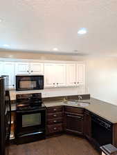 Kitchen featuring black appliances, a sink, white cabinets, dark wood-type flooring, and dark countertops