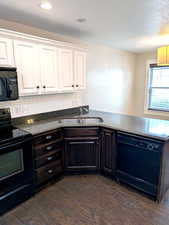 Kitchen featuring black appliances, a sink, dark wood-type flooring, a peninsula, and white cabinetry