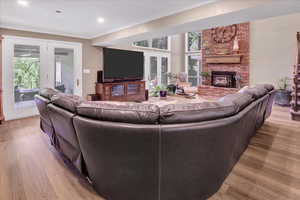 Living area featuring french doors, ornamental molding, wood finished floors, a brick fireplace, and recessed lighting