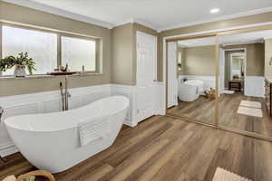 Full bathroom featuring a wainscoted wall, a decorative wall, ornamental molding, a soaking tub, and wood finished floors