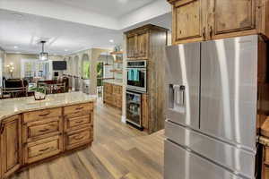 Kitchen featuring stainless steel appliances, wine cooler, arched walkways, light wood finished floors, and brown cabinets