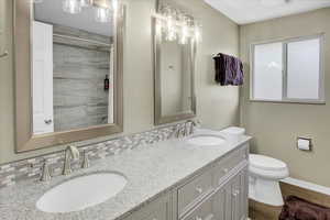 Bathroom featuring toilet, wood finished floors, baseboards, and double vanity